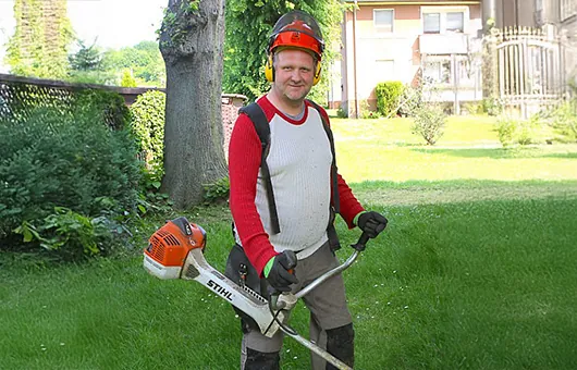 Landschaftsgärtner mit Freischneider bei der Rasenpflege