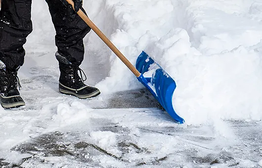 Person räumt Schnee mit einer Schneeschaufel im zuverlässigen Winterdienst